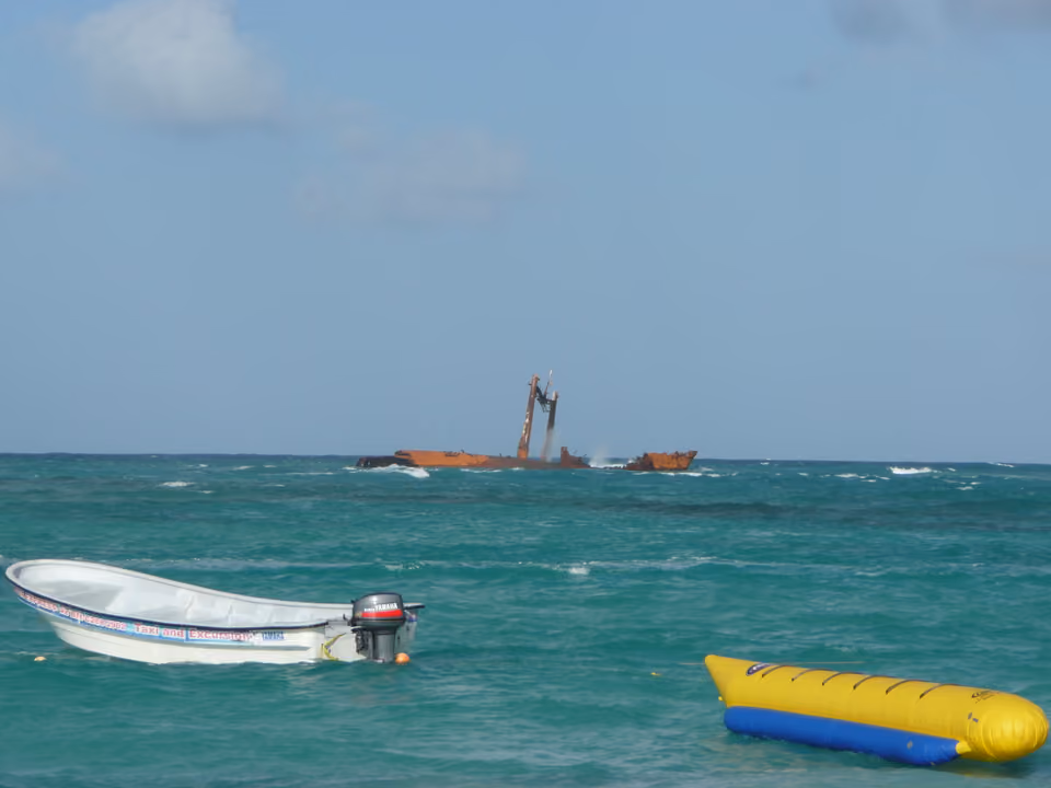 Naufrágio do Astron visível sobre a água perto da costa de Punta Cana, com um barco e uma boia inflável em primeiro plano