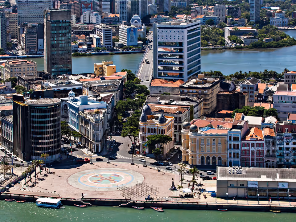 Vista aérea do Marco Zero em Recife, com o piso circular da rosa dos ventos pintado na praça, o casario colonial colorido do Recife Antigo e a ponte sobre o rio ao fundo