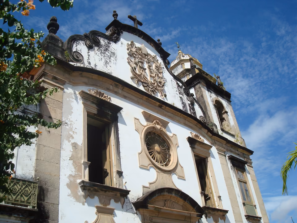 Detalhe da fachada colonial do Mosteiro de São Bento em Olinda, com o frontão barroco esculpido, o óculo circular e a torre sineira ao fundo