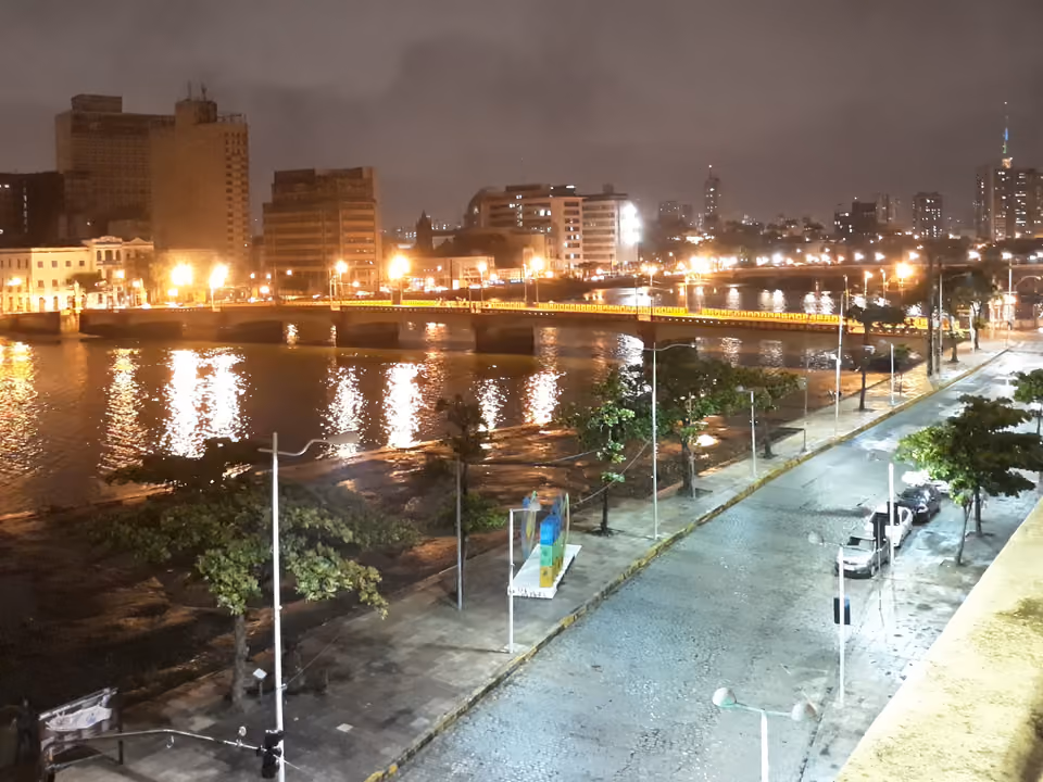 Vista noturna do Rio Capibaribe em Recife, com a Ponte Maurício de Nassau iluminada e as luzes da cidade refletidas na água