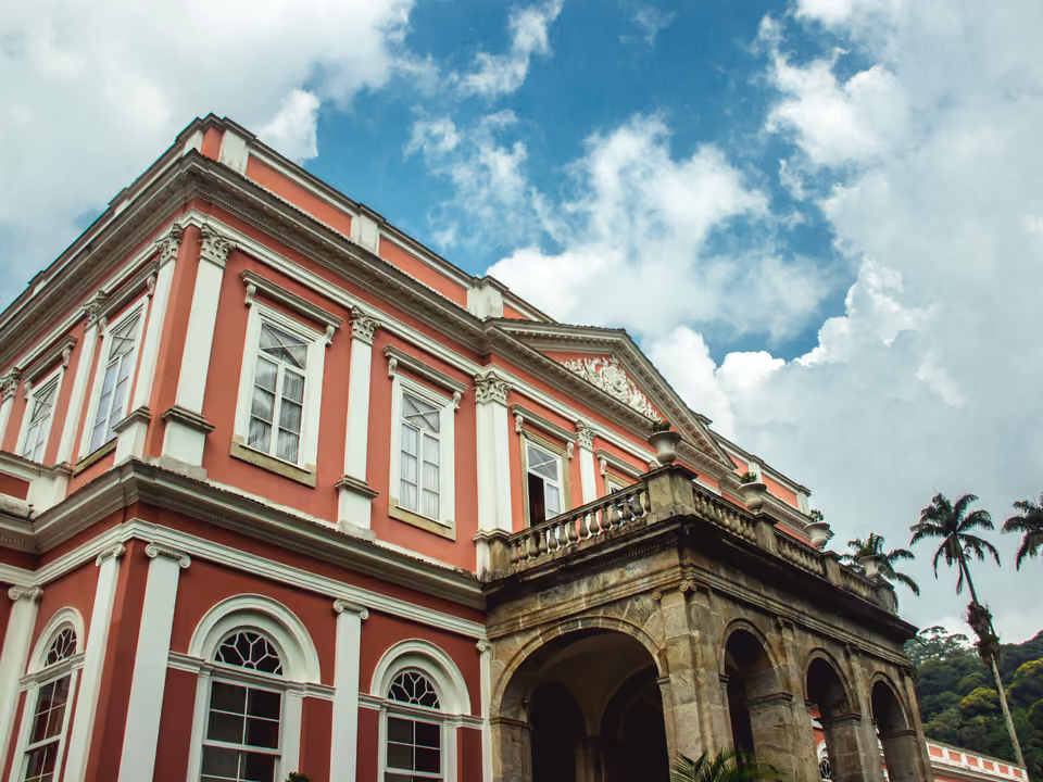 O Museu Imperial de Petrópolis, o antigo palácio de verão de Dom Pedro II, fachada neoclássica cor-de-rosa e branca com pórtico de pedra em arco, entre palmeiras
