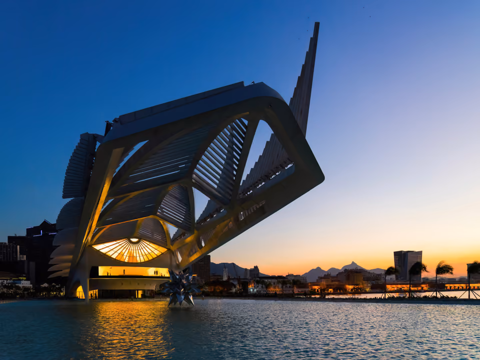O Museu do Amanhã no Rio de Janeiro ao anoitecer, a estrutura branca de espinhas em balanço de Santiago Calatrava iluminada e refletida no espelho d'água da Praça Mauá