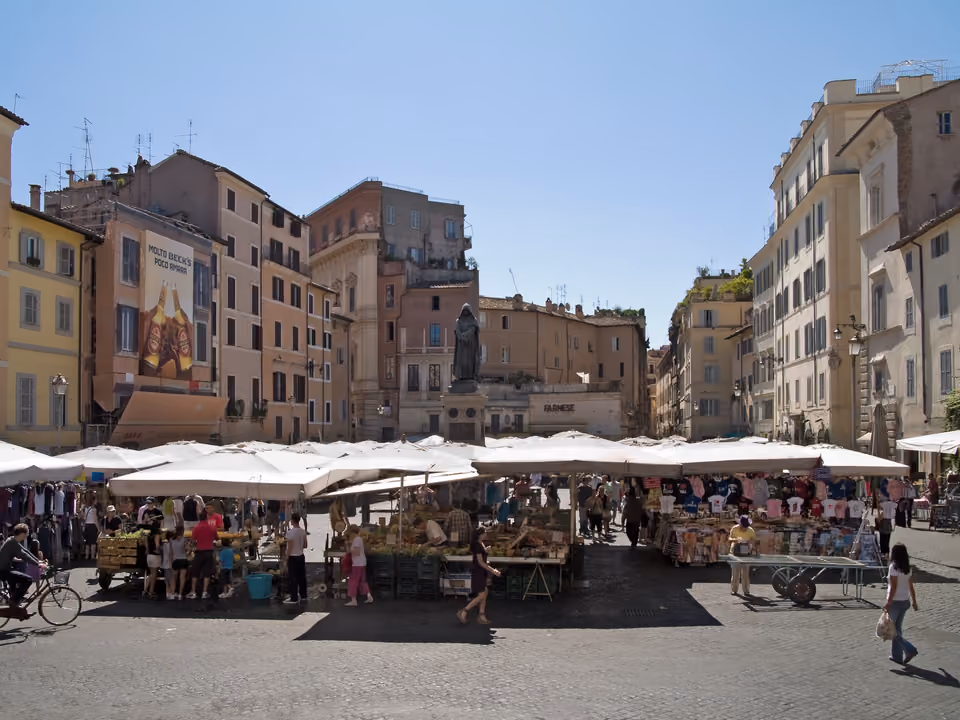 Campo de' Fiori em Roma pela manhã, com as barracas coloridas da feira de frutas e flores e a estátua de Giordano Bruno ao fundo