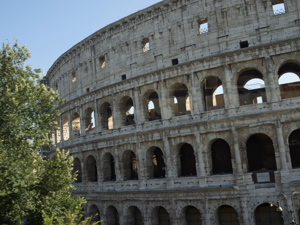 Fachada externa do Coliseu de Roma, o anfiteatro romano com os arcos em três níveis parcialmente preservados sob céu azul