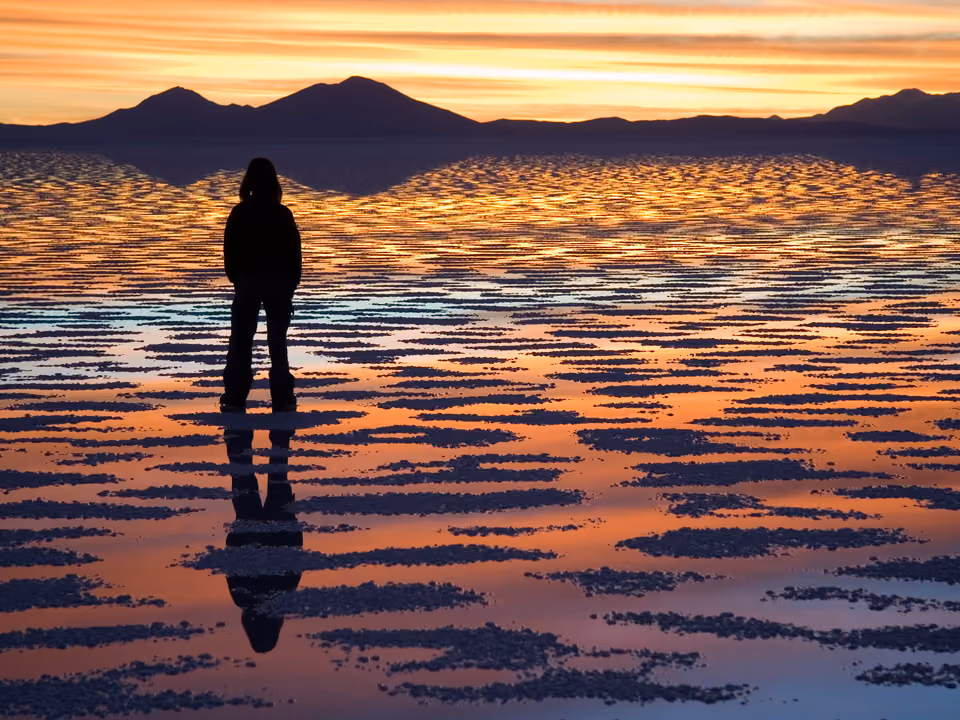 Silhueta de pessoa contra o pôr do sol refletido no Salar de Uyuni, Bolívia