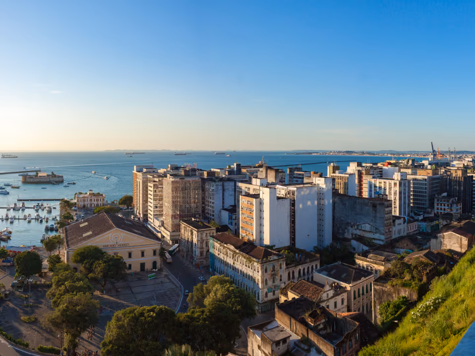 O Mercado Modelo amarelo na Cidade Baixa de Salvador visto do alto, com a Baía de Todos-os-Santos, o Forte de São Marcelo e os guindastes do porto ao fundo