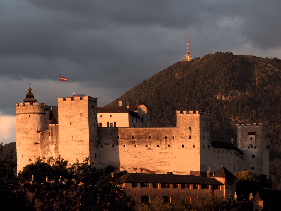 Fortaleza de Hohensalzburg ao entardecer, com colina verde ao fundo, Áustria