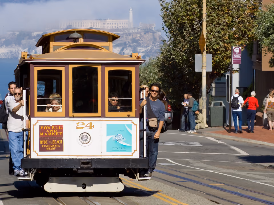 Bonde histórico (cable car) subindo uma rua íngreme em San Francisco, com passageiros pendurados na lateral
