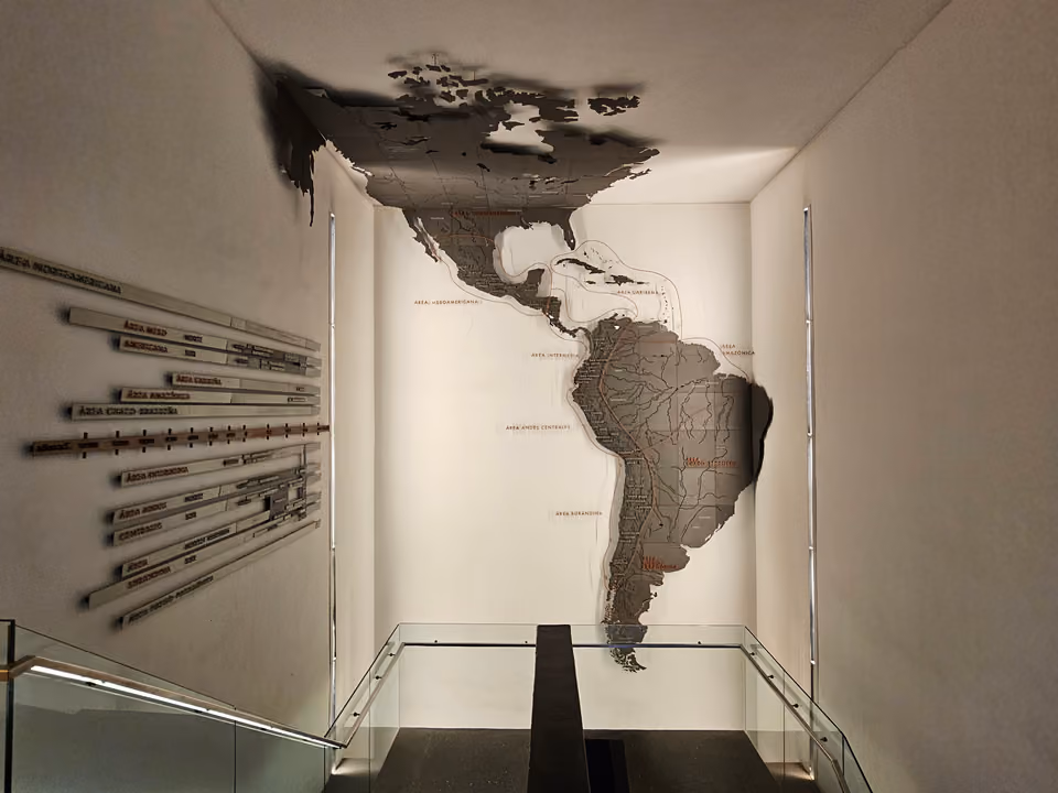 Escadaria interna do Museo Chileno de Arte Precolombino, com um mapa escultórico das Américas na parede marcando as áreas culturais pré-colombianas