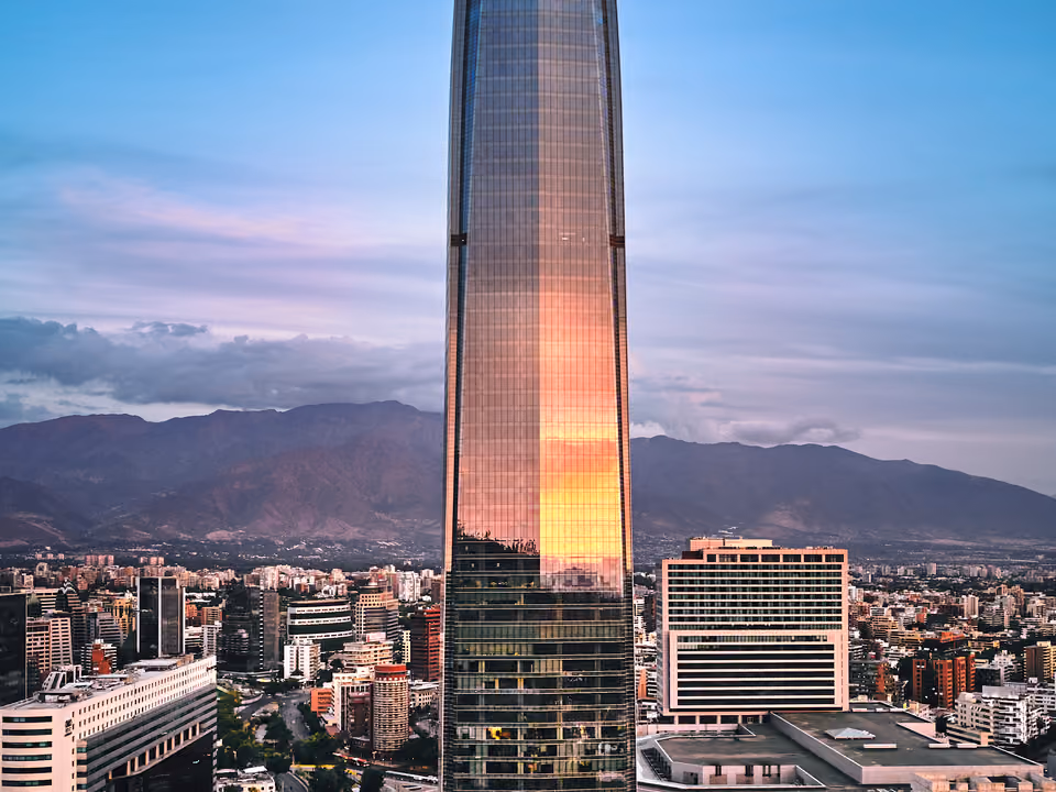 A Gran Torre Santiago, o arranha-céu mais alto da América do Sul, com o pôr do sol refletido nas fachadas de vidro e a cidade ao redor