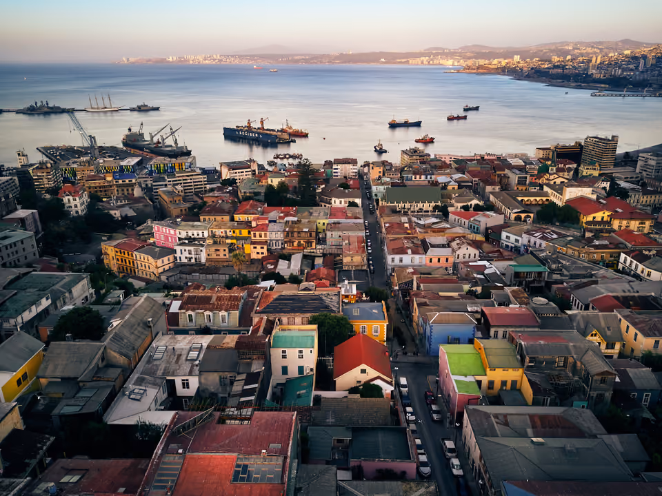Vista do alto de Valparaíso, com os telhados coloridos dos morros descendo até a baía e navios ancorados no porto
