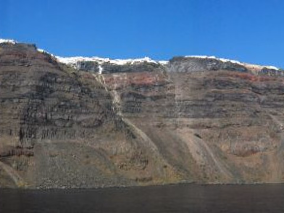 Falésia vulcânica em camadas na borda da caldeira de Santorini, com casas brancas visíveis no topo