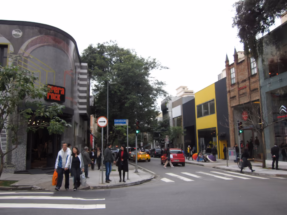 Esquina arborizada da Rua Oscar Freire, nos Jardins, em São Paulo, com lojas de design, vitrines e pedestres atravessando a faixa