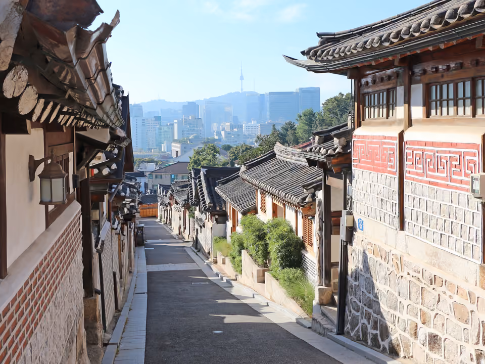 Ruela de casas tradicionais hanok no Bukchon Hanok Village, com o skyline de Seul ao fundo