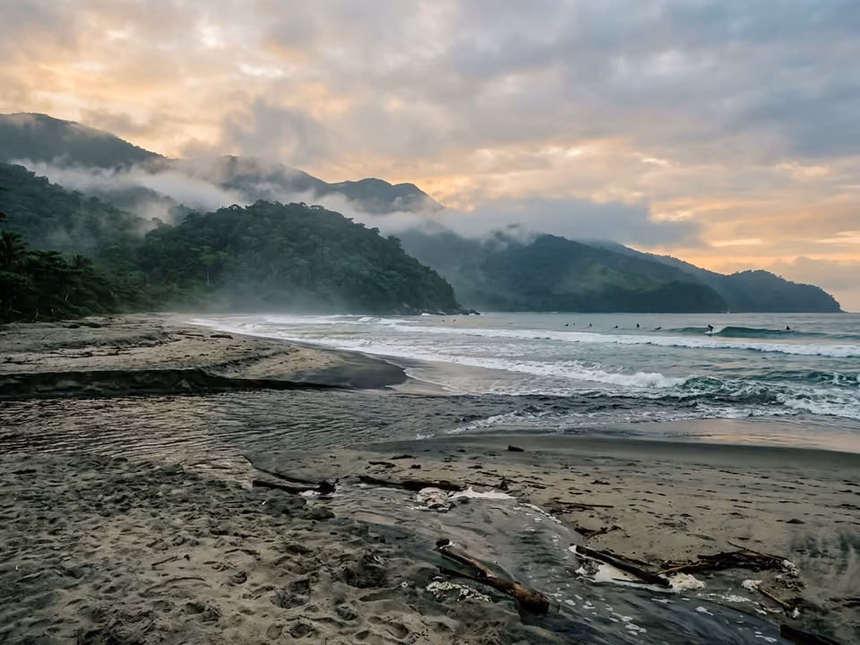 Amanhecer em Itamambuca com silhuetas de surfistas, rio encontrando o mar e névoa nos morros