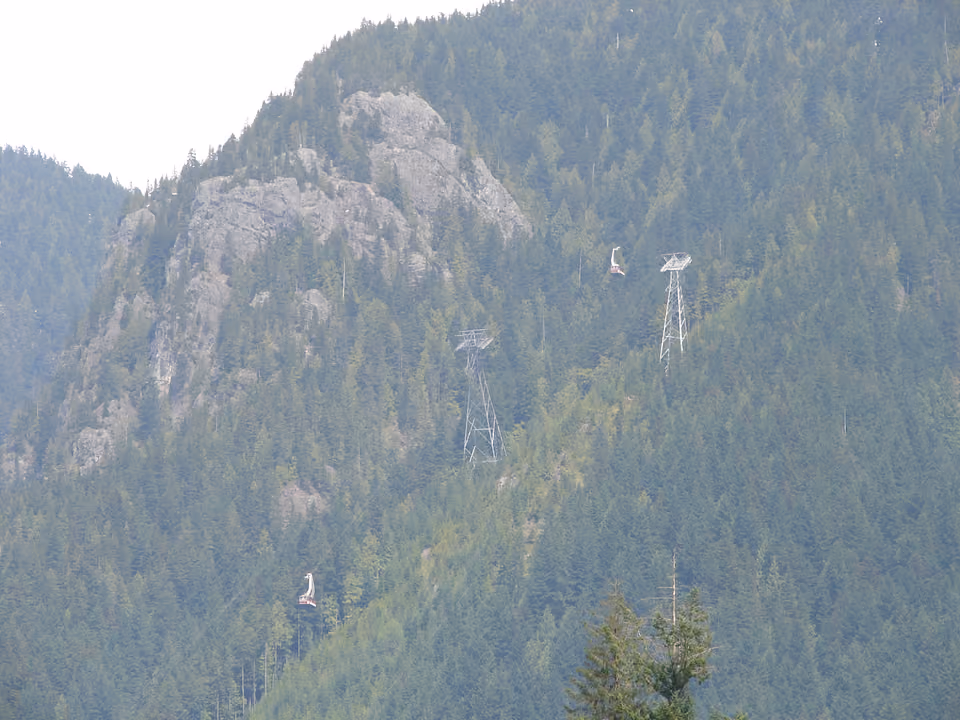 Cabines da gôndola de Grouse Mountain suspensas sobre a floresta, vistas de longe subindo a montanha