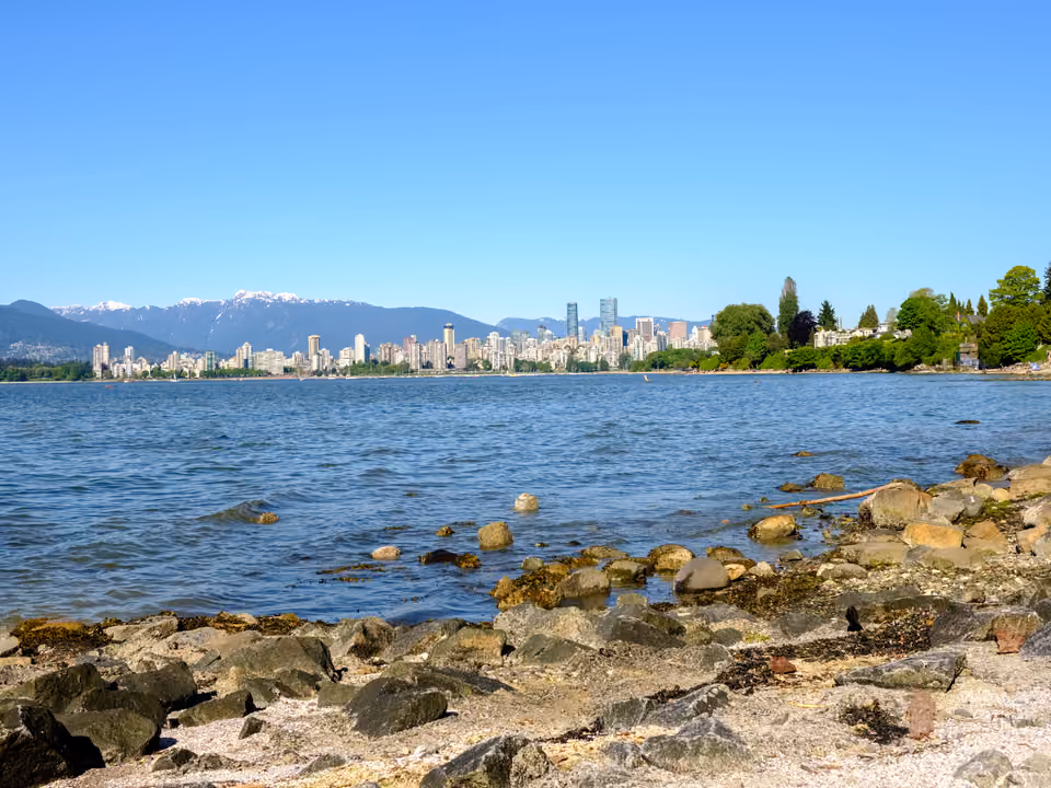 Orla rochosa à beira-mar em Vancouver, com o horizonte de prédios e as montanhas nevadas ao fundo