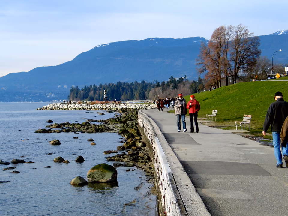 Trilha arborizada dentro de Stanley Park, em Vancouver, com árvores altas e o caminho do Seawall
