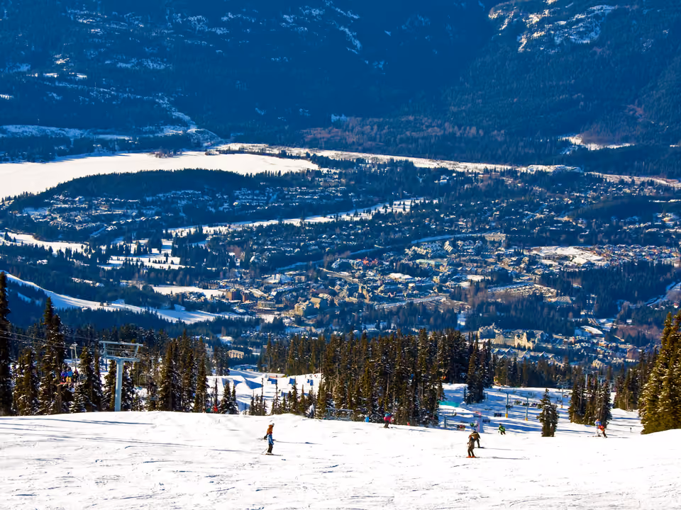 Esquiadores descendo uma pista nevada em Whistler, com a vila e o vale ao fundo