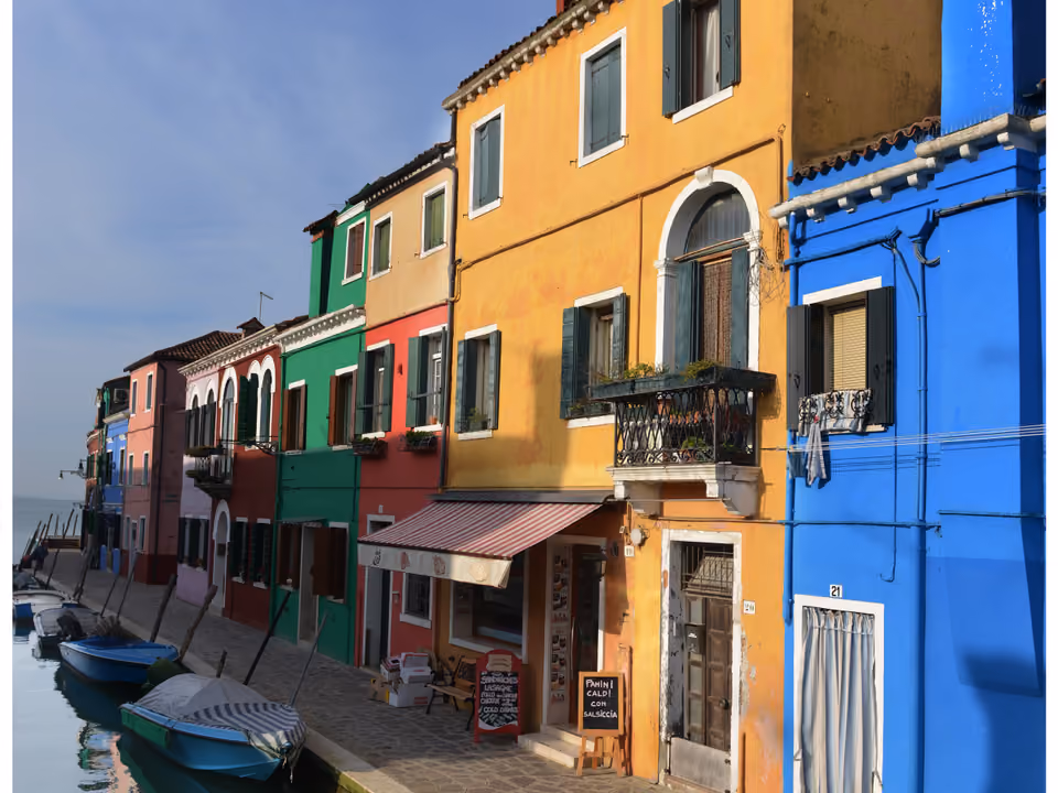 Canal da ilha de Burano perto de Veneza, ladeado por casas pintadas em cores vibrantes e diferentes