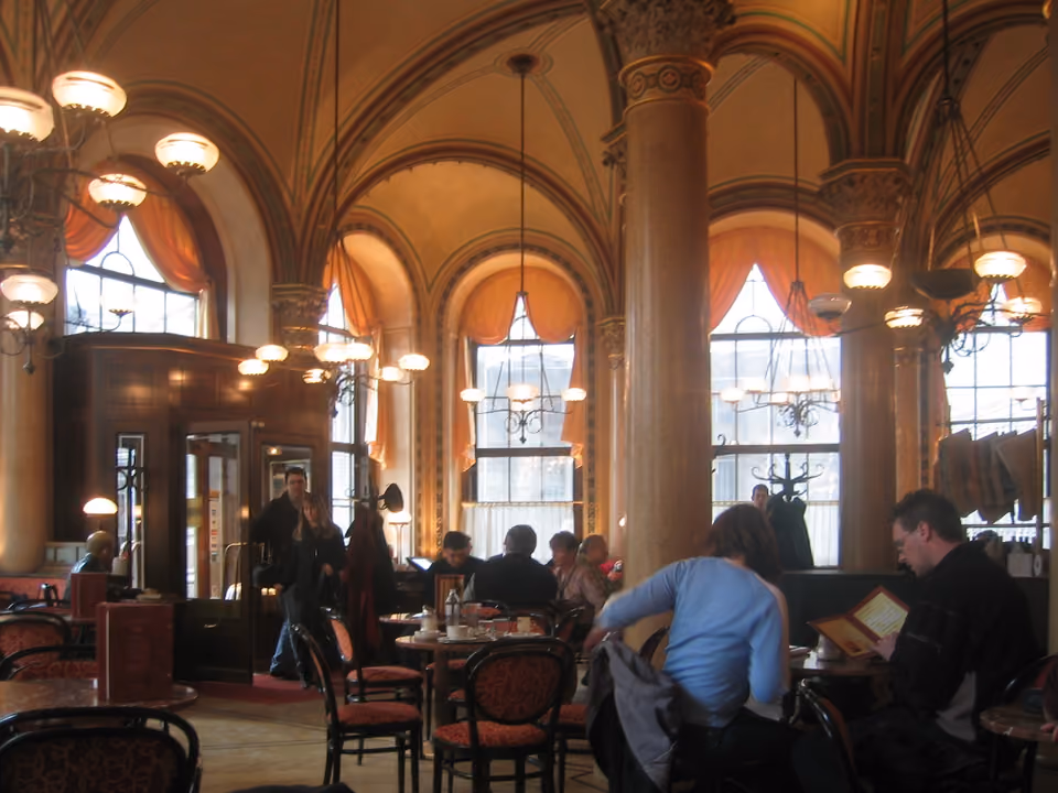 Interior de um café histórico vienense, com mesas de mármore, cadeiras de madeira curvada e lustres clássicos